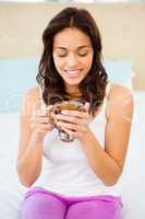 Happy woman holding cup of tea while sitting on bed