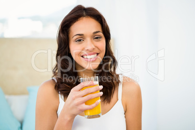 Happy woman holding glass of orange juice while sitting on bed