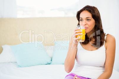 Happy woman holding glass of orange juice while sitting on bed