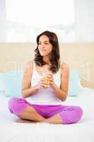 Happy woman holding glass of orange juice while sitting on bed