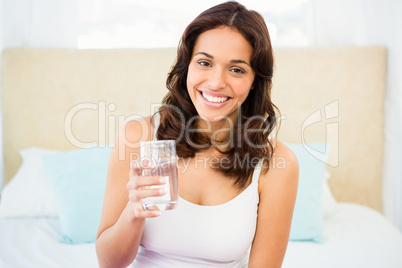 Happy woman holding glass of water while sitting on bed