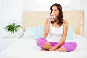 Happy woman holding glass of water while sitting on bed