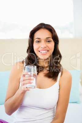 Happy woman holding glass of water while sitting on bed