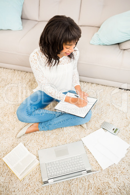 Casual woman writing notes while using laptop