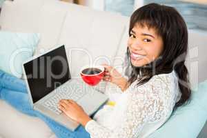 Casual woman using her laptop while holding coffee