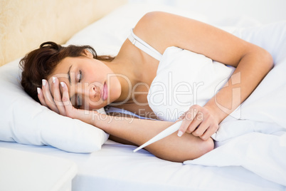 Woman holding her head and a thermometer