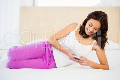 Pretty woman using her phone while lying on the bed