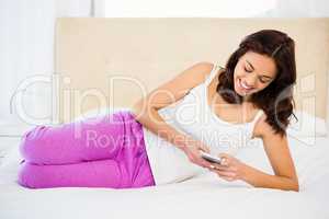 Pretty woman using her phone while lying on the bed