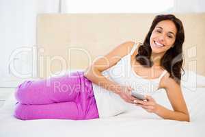 Pretty woman using her phone while lying on the bed