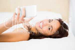 Pretty woman using her phone while lying on the bed