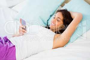 Pretty woman using her phone while lying on the bed