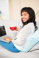Smiling woman with coffee cup using laptop