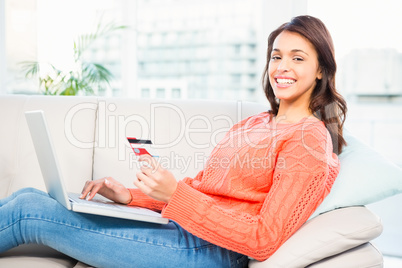 Smiling woman with a credit card and a laptop on a sofa