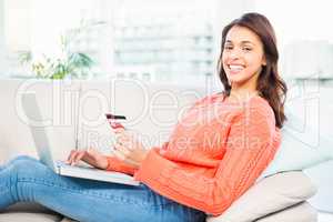 Smiling woman with a credit card and a laptop on a sofa
