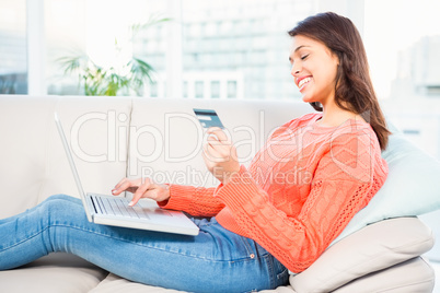 Smiling woman with a credit card and a laptop on a sofa