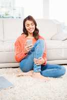 Smiling woman using smartphone while sitting on floor