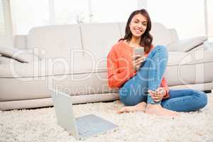 Smiling woman using smartphone while sitting on floor