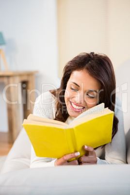 Peaceful woman lying on couch reading a book