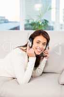 Pretty woman listening with headphones to music lying on couch