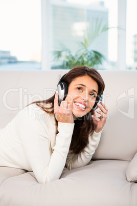 Pretty woman listening with headphones to music lying on couch