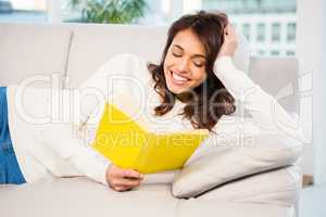 Peaceful woman lying on couch reading a book