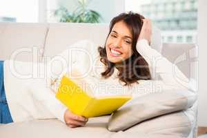 Peaceful woman lying on couch reading a book