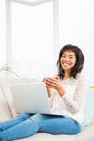 Smiling woman relaxing on couch with coffee using laptop