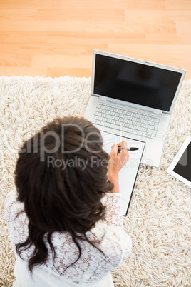 Above view of a woman writing note while using her laptop