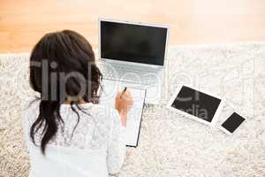 Above view of a woman writing note while using her laptop