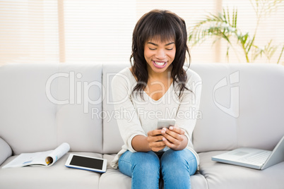 Pretty brunette sitting on her couch using her smartphone