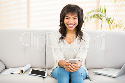 Pretty brunette sitting on her couch using her smartphone