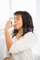 Pretty woman using inhaler on couch
