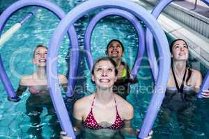 Happy fitness class doing aqua aerobics with foam rollers