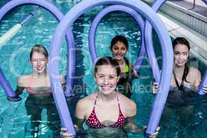 Happy fitness class doing aqua aerobics with foam rollers