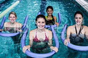 Happy fitness class doing aqua aerobics with foam rollers