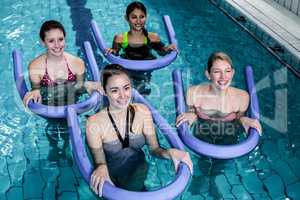 Happy fitness class doing aqua aerobics with foam rollers