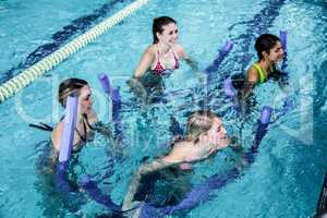 Happy fitness class doing aqua aerobics with foam rollers