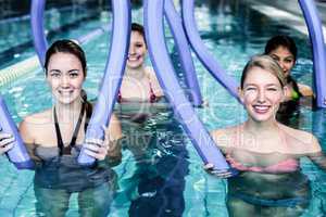 Happy fitness class doing aqua aerobics with foam rollers