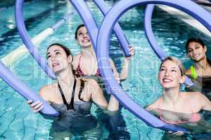 Happy fitness class doing aqua aerobics with foam rollers