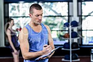Muscular trainer writing on clipboard