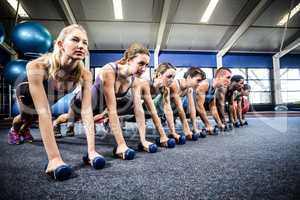 Fitness class in plank position with dumbbells