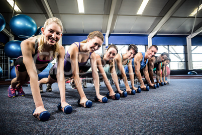 Fitness class in plank position with dumbbells