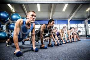 Fitness class in plank position with dumbbells