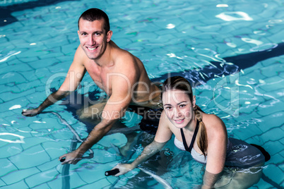 Smiling couple cycling in the pool