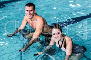 Smiling couple cycling in the pool