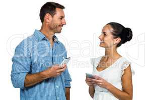 Smiling couple holding smartphones and looking at each other