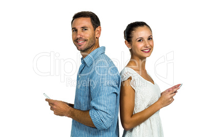 Smiling couple standing back to back using smartphones