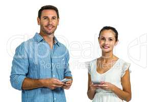 Smiling couple using smartphones and looking at camera
