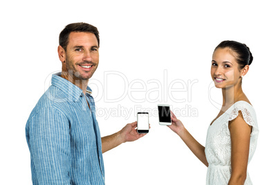 Smiling couple holding smartphones and looking back at camera