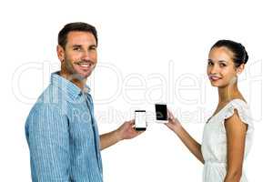 Smiling couple holding smartphones and looking back at camera